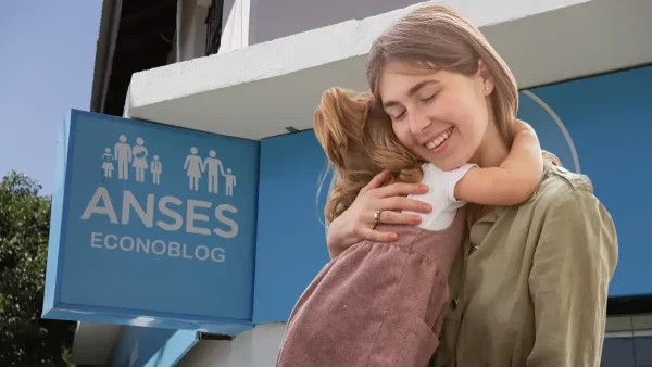 Madre abrazada a su hija junto a un cartel de Anses para AUH y SUAF