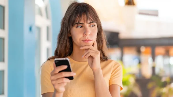 Mujer pensando con su celular en una tienda